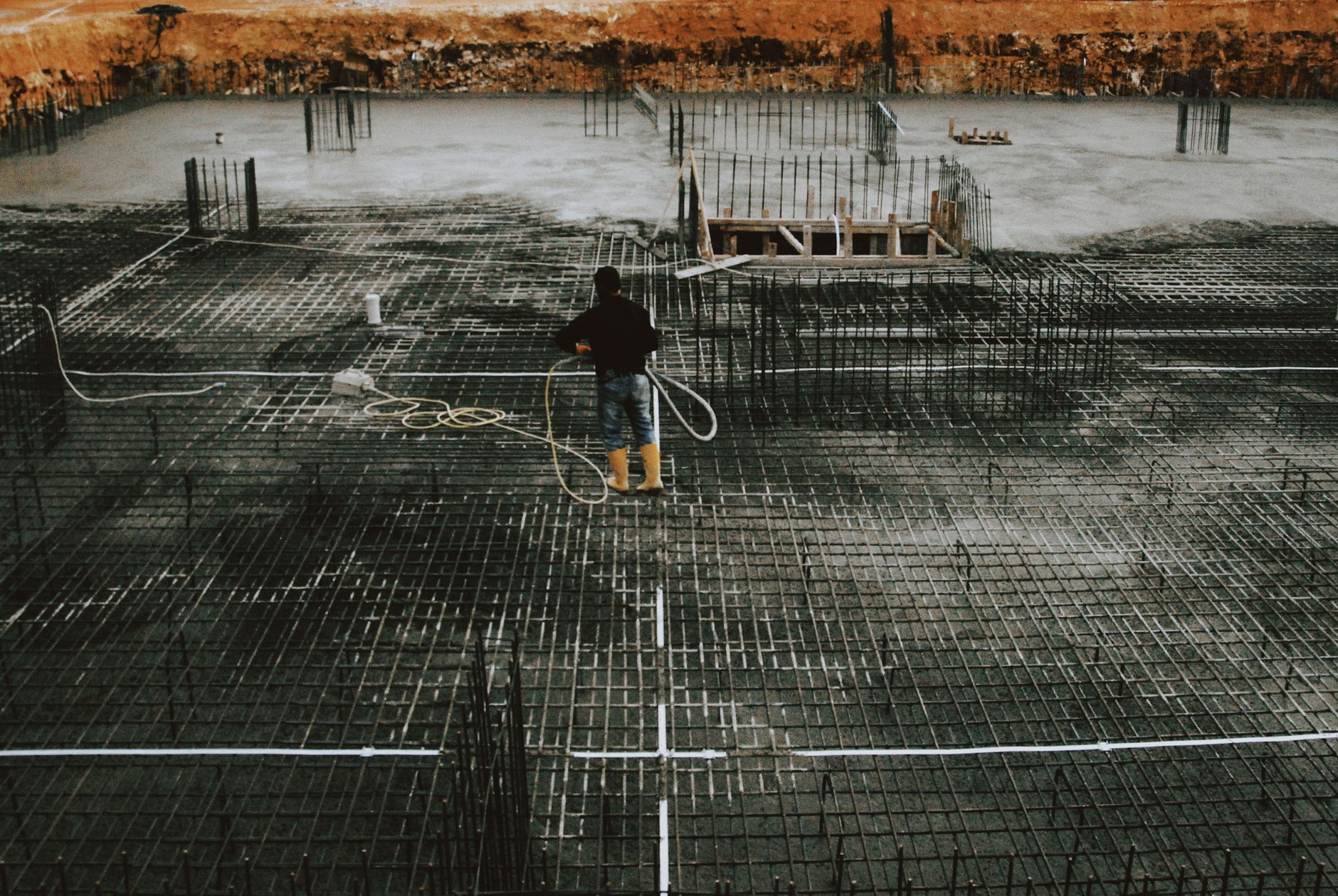A worker stands on a reinforced concrete foundation, preparing for construction.