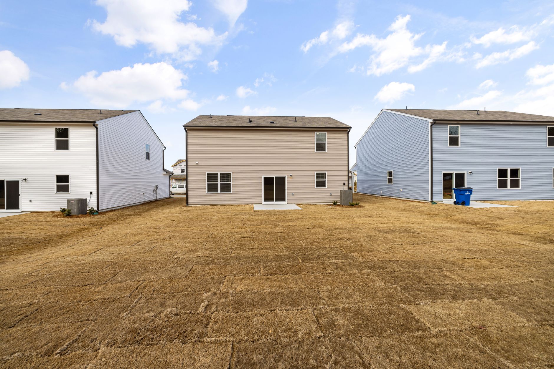 A row of modern suburban homes with freshly laid dry lawns under a bright sky.