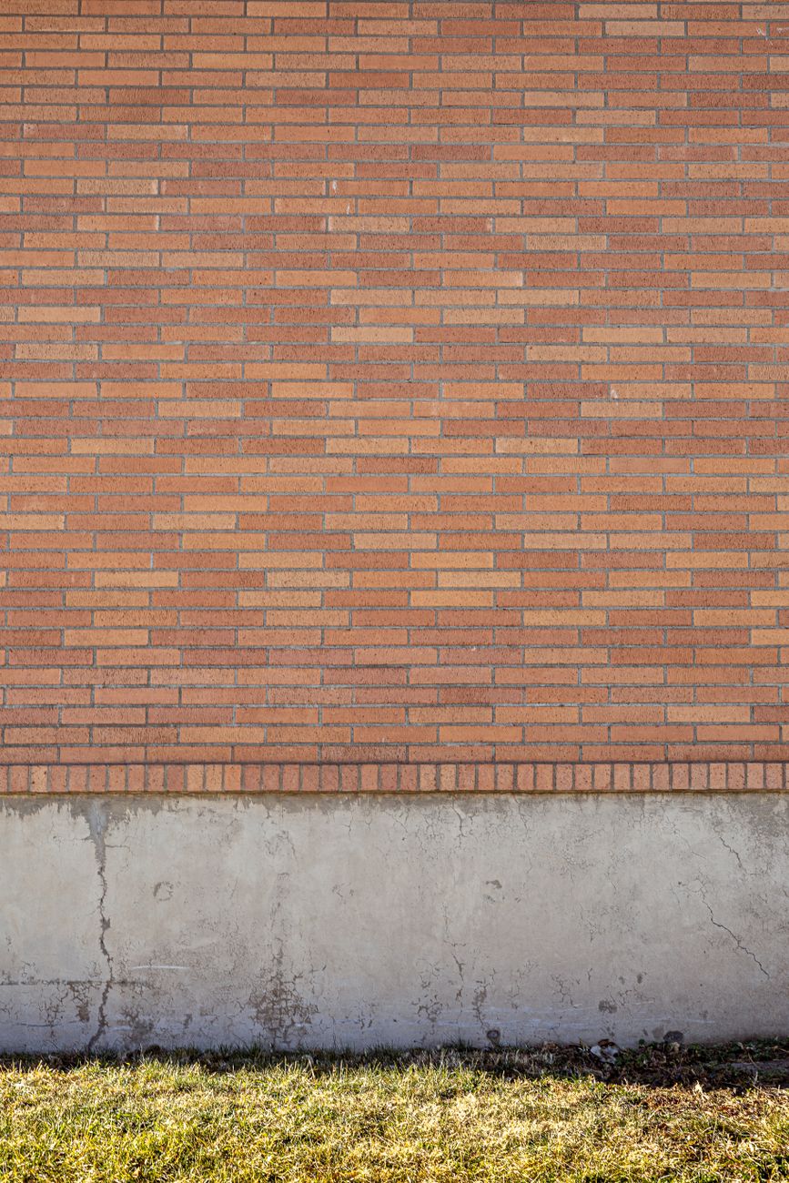 Simple red brick wall with contrasting concrete foundation and grass foreground